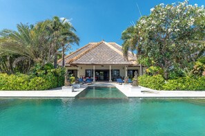 Un complexe hôtelier doté d’une piscine, de chaises longues et d’un aménagement paysager de style tropical.