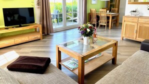 En moderne stue med fjernsyn, sofa, sofabord og et spiseområde med stole og et bord.