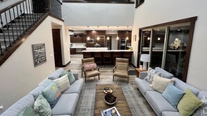 Uma sala de estar ampla com teto alto, escada, cozinha com ilha central e área de estar com sofás e mesa de centro.