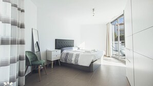 Een moderne slaapkamer met een bed, nachtkastje, stoel en een groot raam.