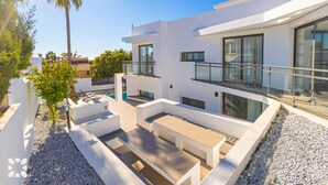 Een modern huis met twee verdiepingen, een plat dak, grote ramen en een terras met zitplaatsen.