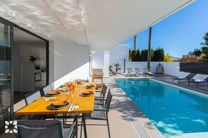 Un espace de repas extérieur moderne, doté d’une piscine, de chaises longues et offrant une vue dégagée sur le ciel.