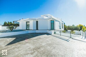 Un bâtiment moderne de couleur blanche, doté d’un toit plat, de grandes fenêtres et d’un patio en béton.