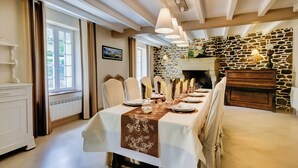 Une salle à manger avec une longue table dressée pour le repas, un mur en pierre et une cheminée.