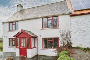 A two-story house with a red door and windows, a chimney, and a solar panel on the roof.