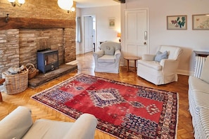 A cozy living room with a stone fireplace, a red patterned rug, and comfortable seating. - Host & Stay | Penrheol Farmhouse (Brecon)