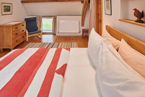 A bedroom with a bed, a wooden dresser, a chair, a radiator, and a window with curtains.