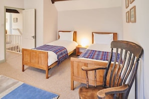 A bedroom with two wooden beds, a wooden chair, and a white door leading to a staircase.