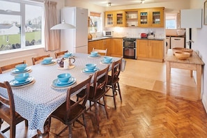 A dining area with a table set for six, wooden chairs, and a view of the kitchen in the background.