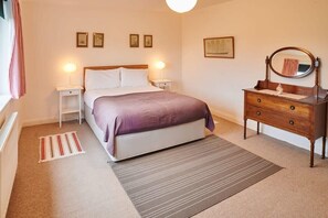 A bedroom with a bed, bedside tables, a dresser, a mirror, and a rug.
