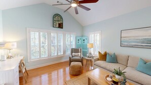 Un salon spacieux avec un plafond haut, de grandes fenêtres, un ventilateur de plafond et une décoration sur le thème de la côte.
