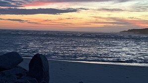 Une plage avec de gros rochers au premier plan et un coucher de soleil sur l’océan.