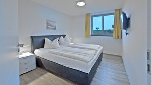 Una camera da letto moderna con un letto grande, comodini, una finestra con tende e un televisore a parete.