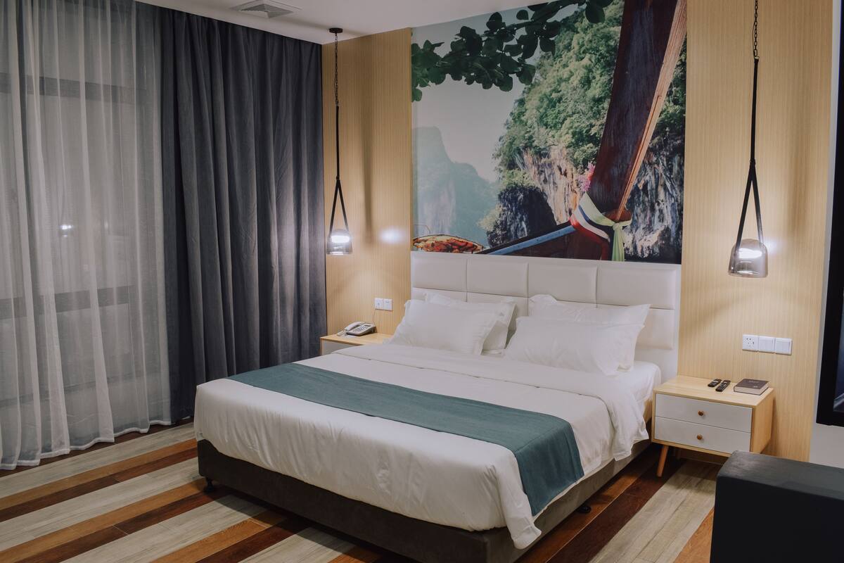A modern hotel room with a large bed, a nightstand, a desk, and a mural on the wall.
