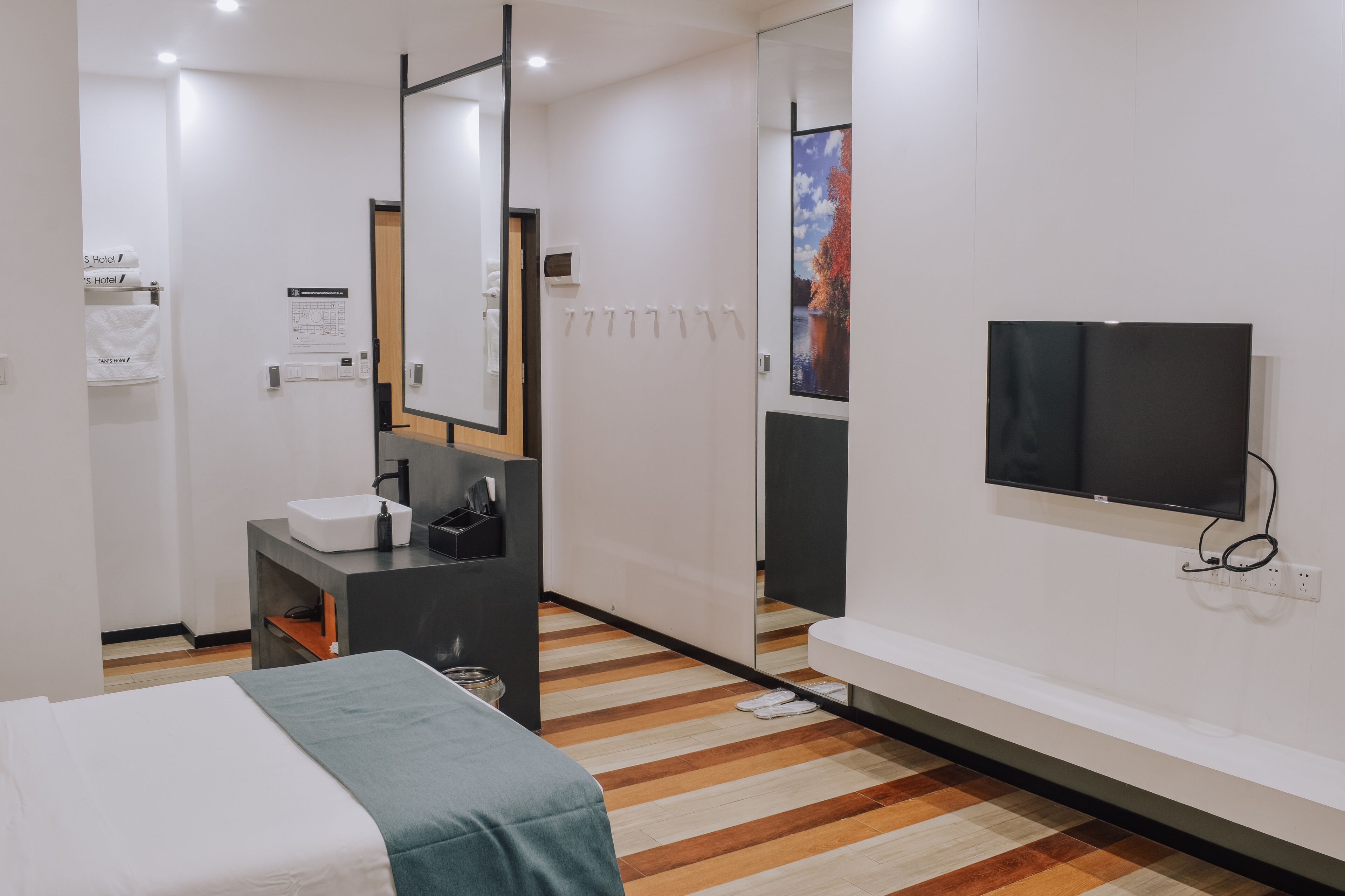 Een moderne hotelkamer met een bed, een badkamer met een wastafel en spiegel, een aan de muur bevestigde televisie en een houten vloer.