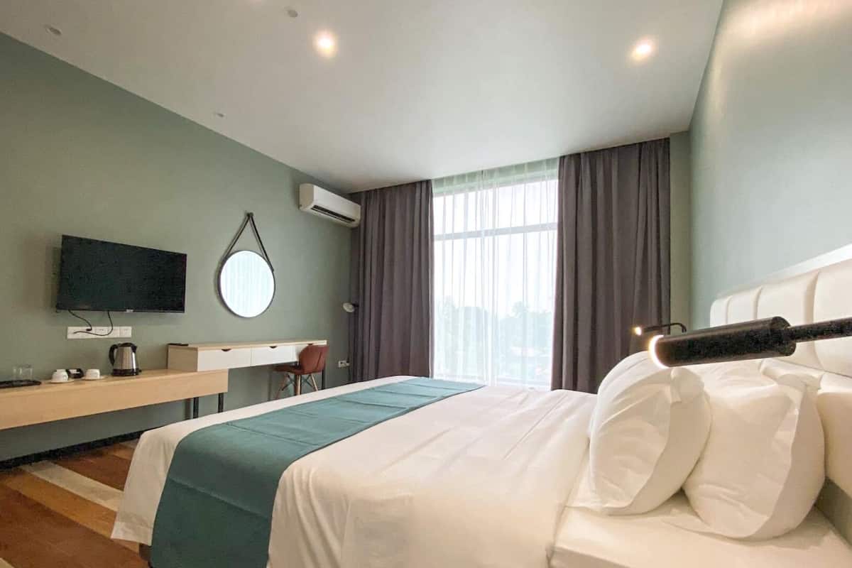 A hotel room with a bed, a desk, a TV, and a window with curtains.