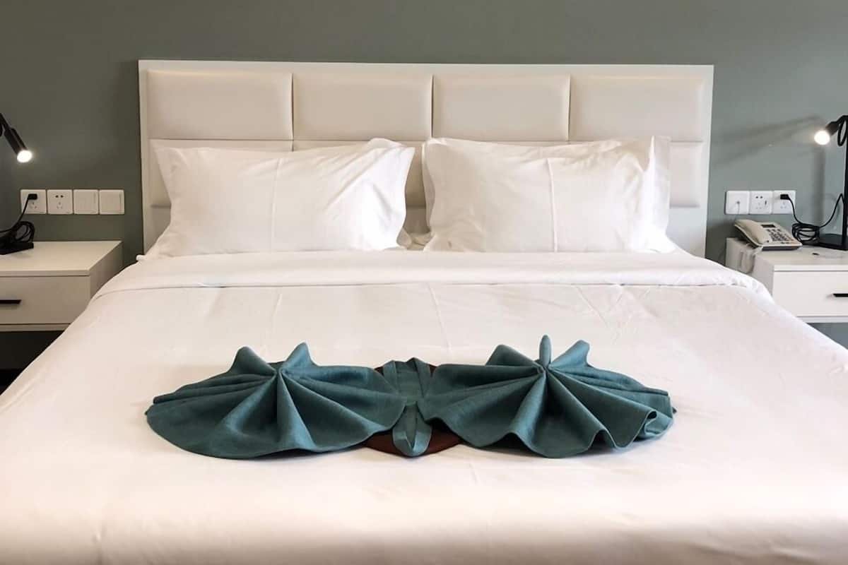 A neatly made bed with white linens and a teal decorative pillow.