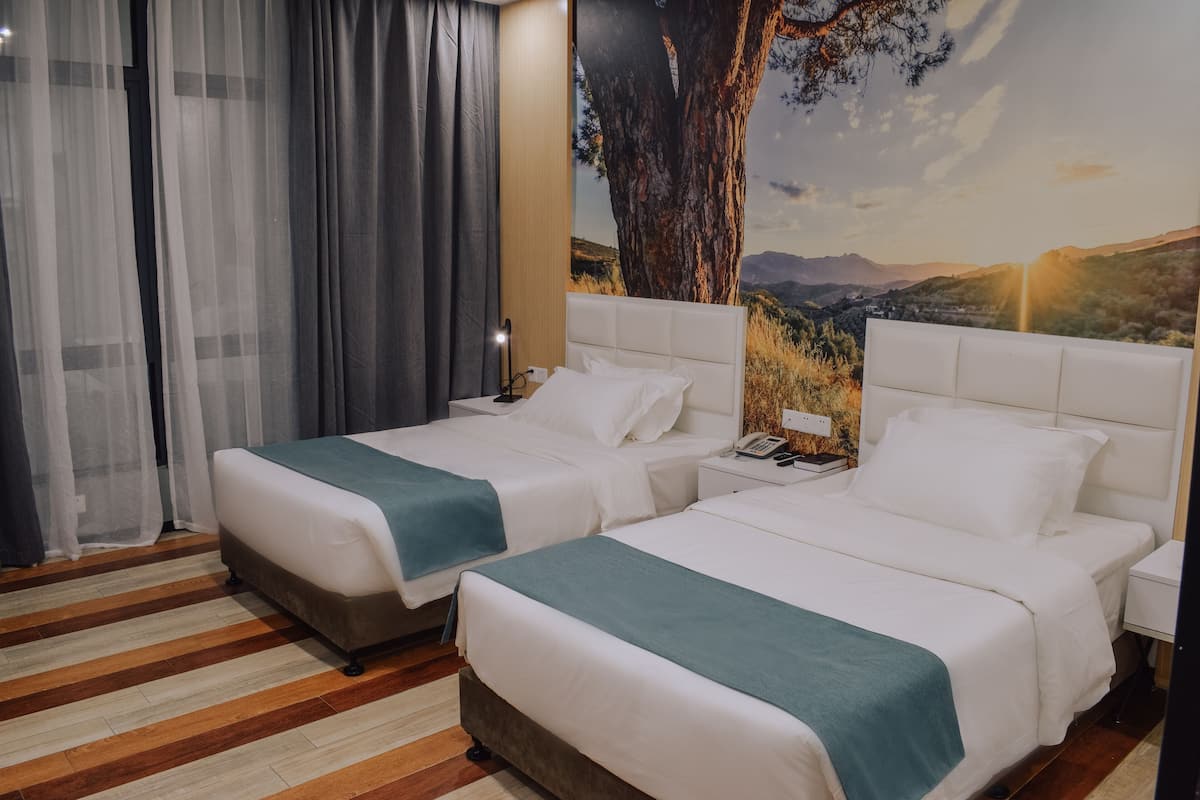 A hotel room with two beds, a large tree mural on the wall, and a wooden floor.