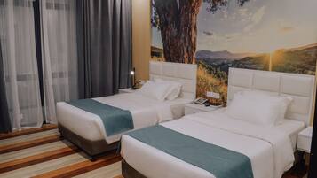 Habitación de hotel con dos camas, un mural grande con un árbol en la pared y piso de madera.