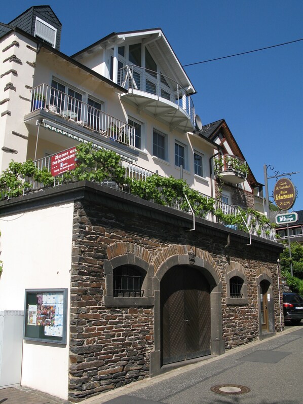 A building with a stone facade, a balcony with white railings, and a sign indicating a restaurant.