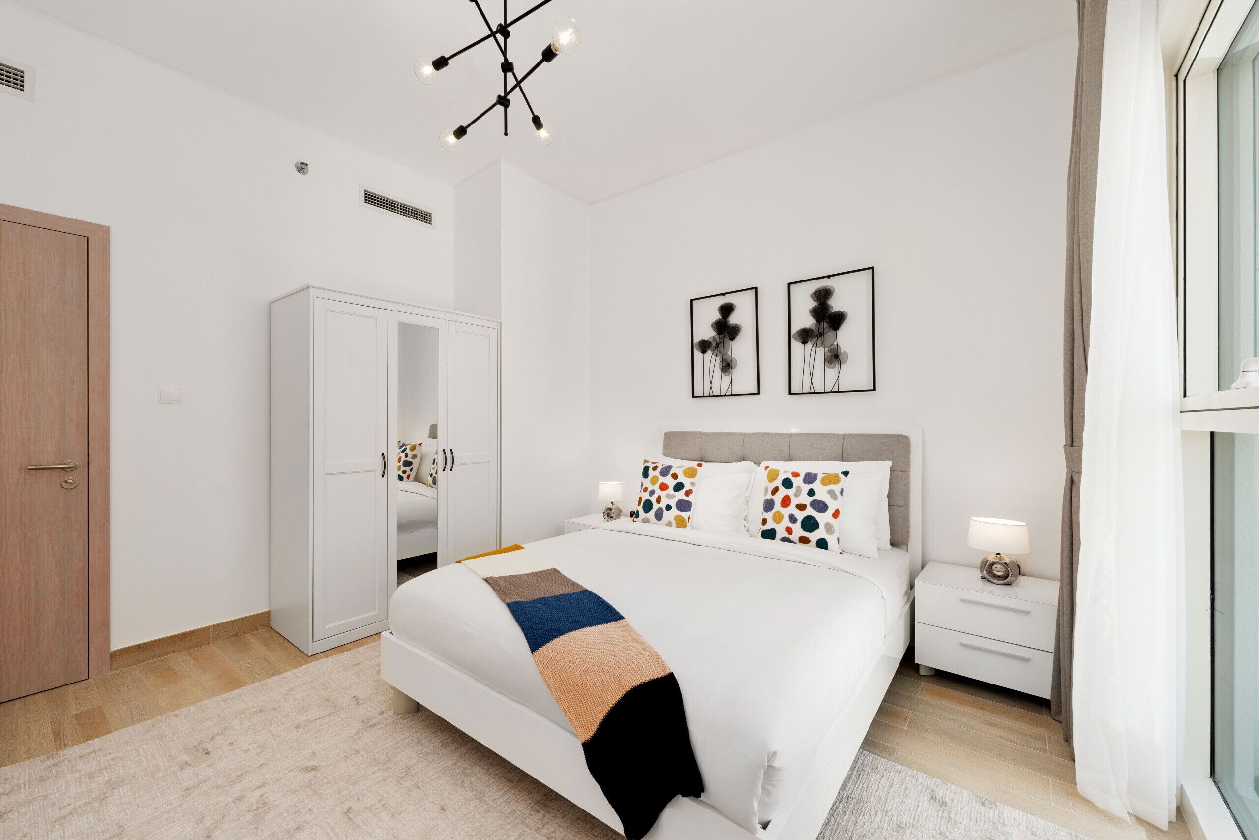 Een moderne slaapkamer met een groot bed, een kledingkast, een nachtkastje en twee kunstwerken aan de muur.
