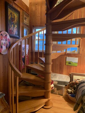 Un intérieur en bois avec un escalier en colimaçon, des œuvres d’art encadrées et une vue par les fenêtres.