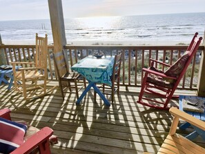 A wooden deck with a table and chairs, overlooking the ocean.
