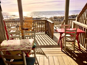 A wooden deck with a table and chairs, overlooking the ocean.
