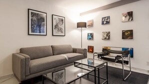 Ein modernes Wohnzimmer mit einem grauen Sofa, einem Glastisch und einer schwarzen Metallbank.