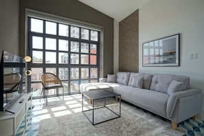 A modern living room with a grey sofa, a coffee table, and a large window offering a view of buildings.