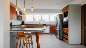 A modern kitchen with wooden cabinets, a central island with stools, stainless steel appliances, and pendant lighting. - w* | Polished 3BR Duplex in Condesa (Ciudad de México)