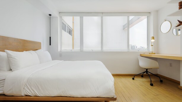 A modern hotel room with a large bed, a desk, and a view of the city through large windows. - w* | Polished 3BR Duplex in Condesa (Ciudad de México)