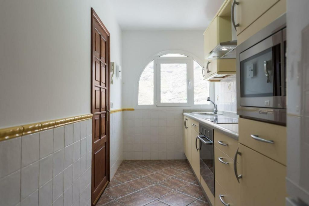 A compact kitchen with a window, white tiled walls, and a tiled floor.