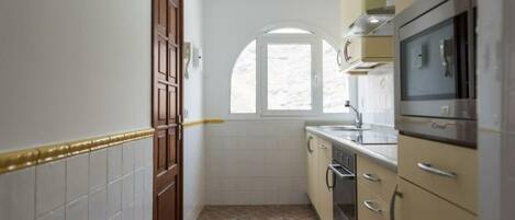 A compact kitchen with a window, white tiled walls, and a tiled floor.