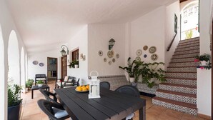 Een eethoek met een houten tafel, stoelen, een bankje en potplanten.