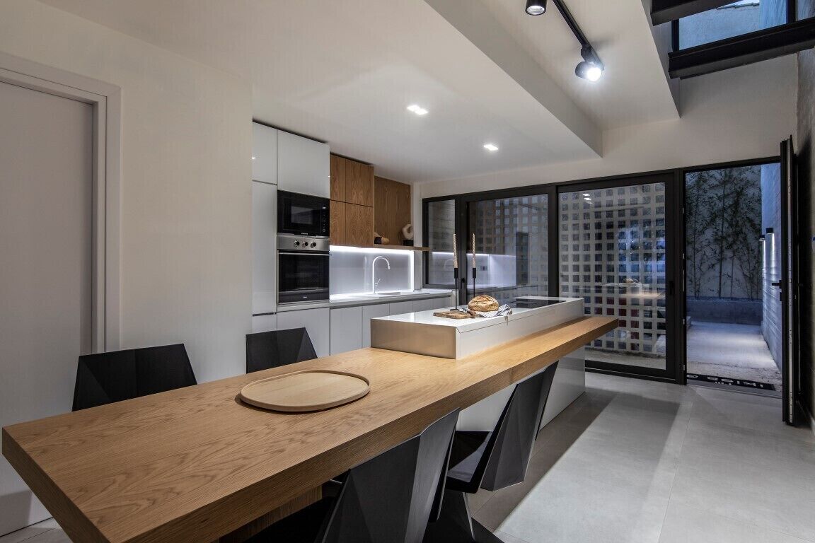 A modern kitchen with a wooden dining table, built-in appliances, and large windows.
