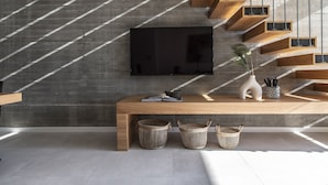Un soggiorno moderno con una grande TV a schermo piatto montata su una parete in cemento, un tavolo consolle in legno e scaffali a muro in legno.