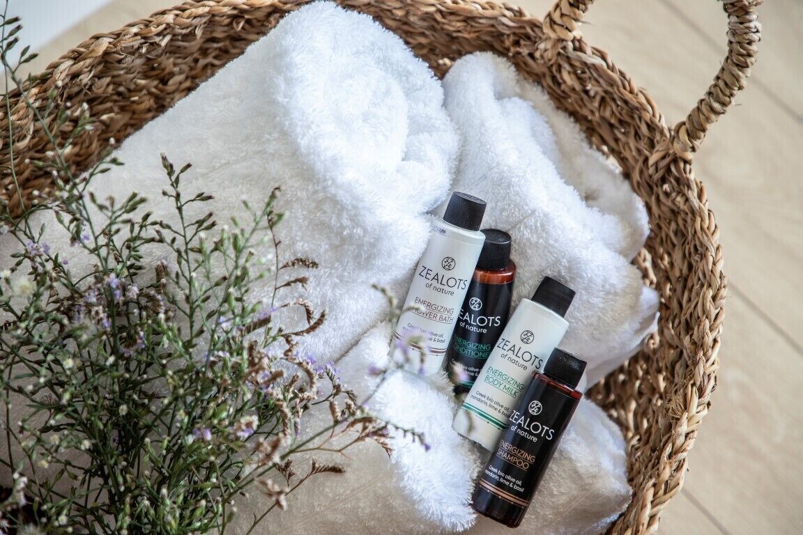 A wicker basket containing white towels, three bottles of Zealots body care products, and some dried flowers.