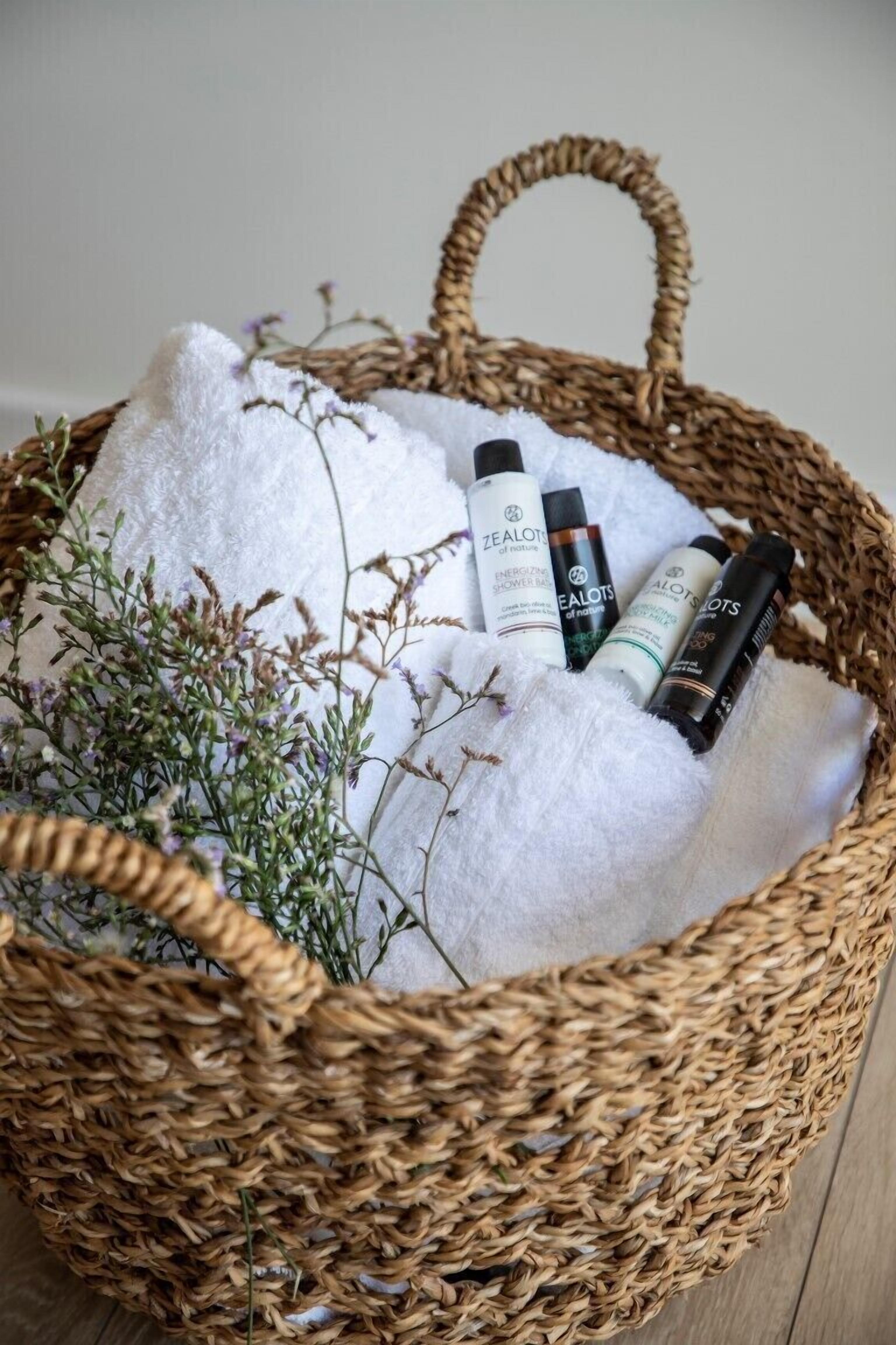Uma cesta de vime com toalhas brancas e produtos de cuidados para a pele Zealot.