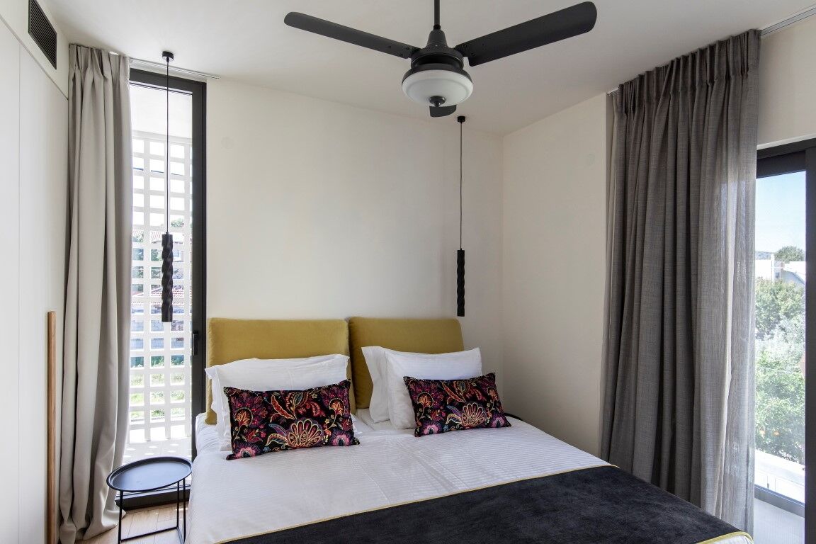 A hotel room with a bed, a ceiling fan, a window with curtains, and a view of the outside.