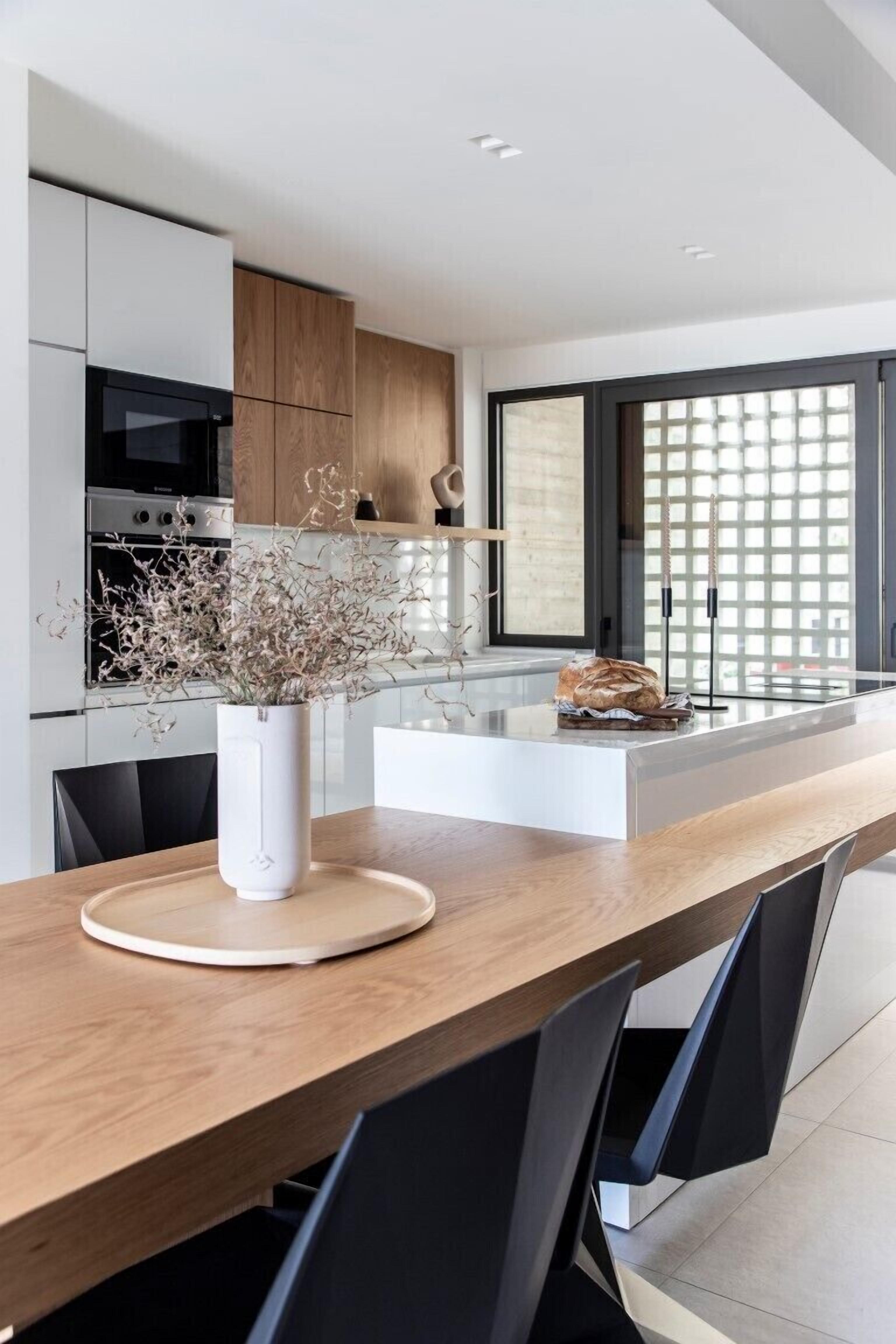 Una cocina moderna con una mesa de comedor de madera, un florero blanco con flores secas y una hogaza de pan sobre la encimera.