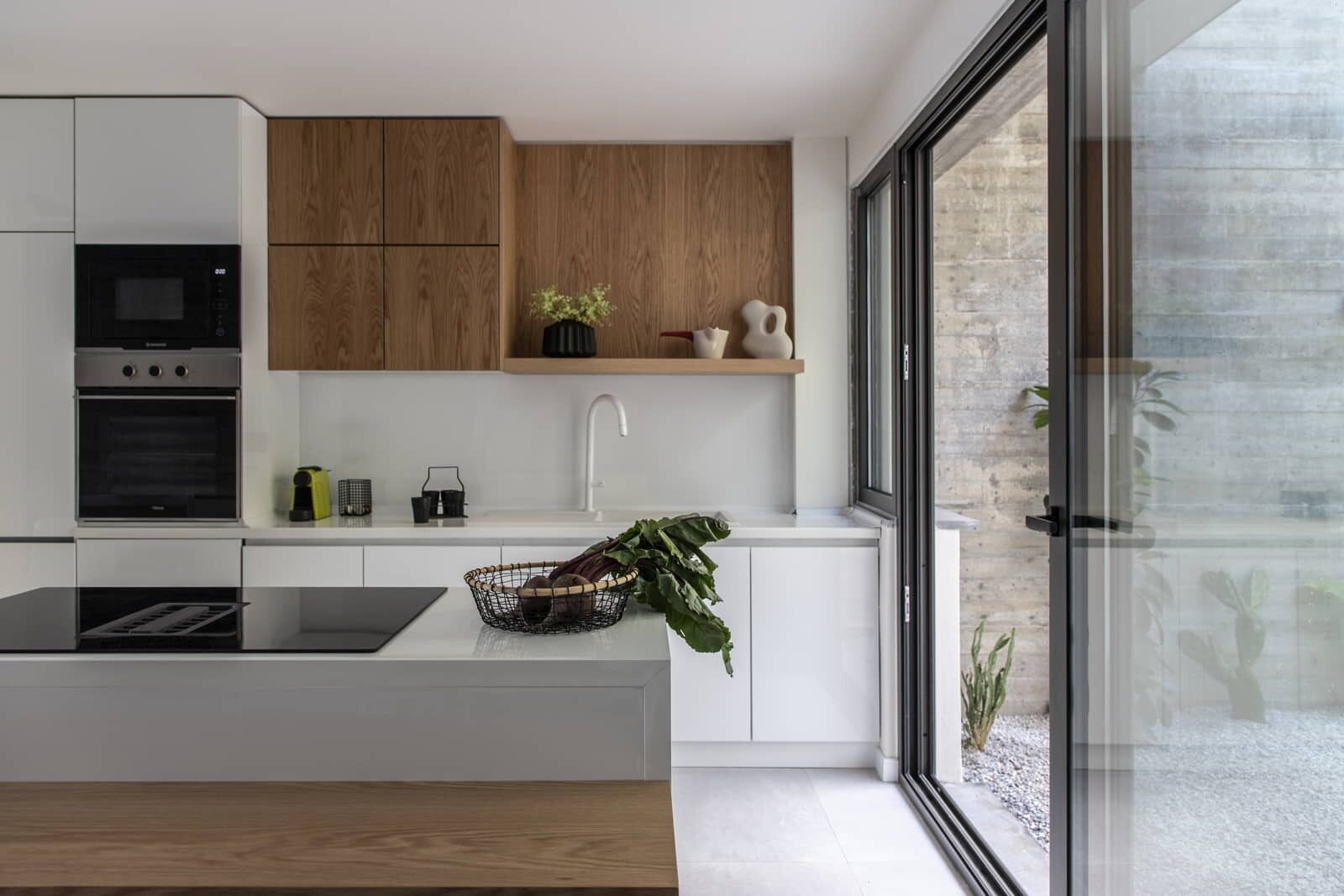 Una cocina moderna con armarios blancos, un revestimiento de pared de madera, horno empotrado y un ventanal con vistas al exterior.