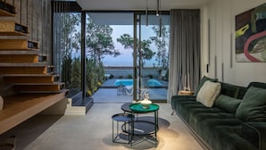 Un soggiorno moderno con un divano verde, un tavolino rotondo e vista su una piscina e alberi.