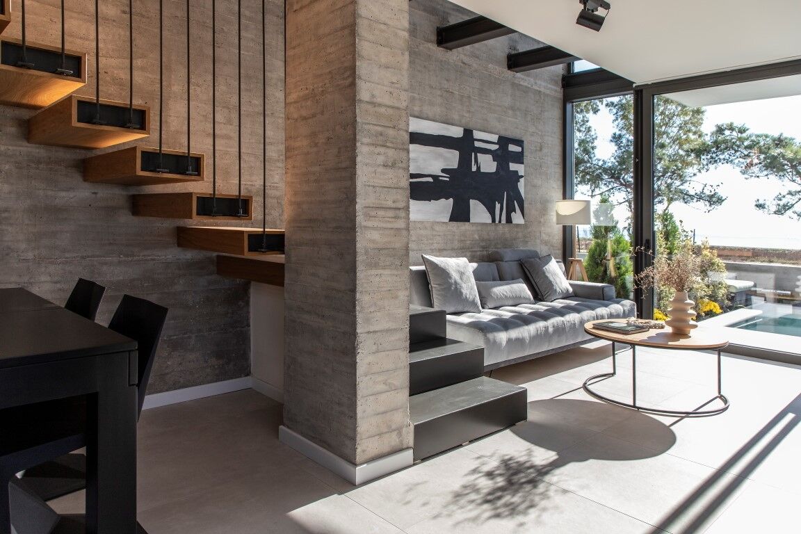 A modern living room with a concrete accent wall, a sofa with cushions, a coffee table, and a dining area with chairs.