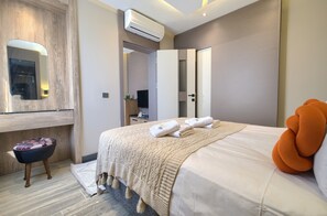 Una habitación de hotel moderna con una cama grande, un televisor de pantalla plana, un espejo y un equipo de aire acondicionado.