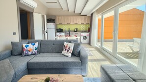 Ein modernes Wohnzimmer mit grauem Sofa, einem Holztisch und einem großen Fenster mit Ausblick.