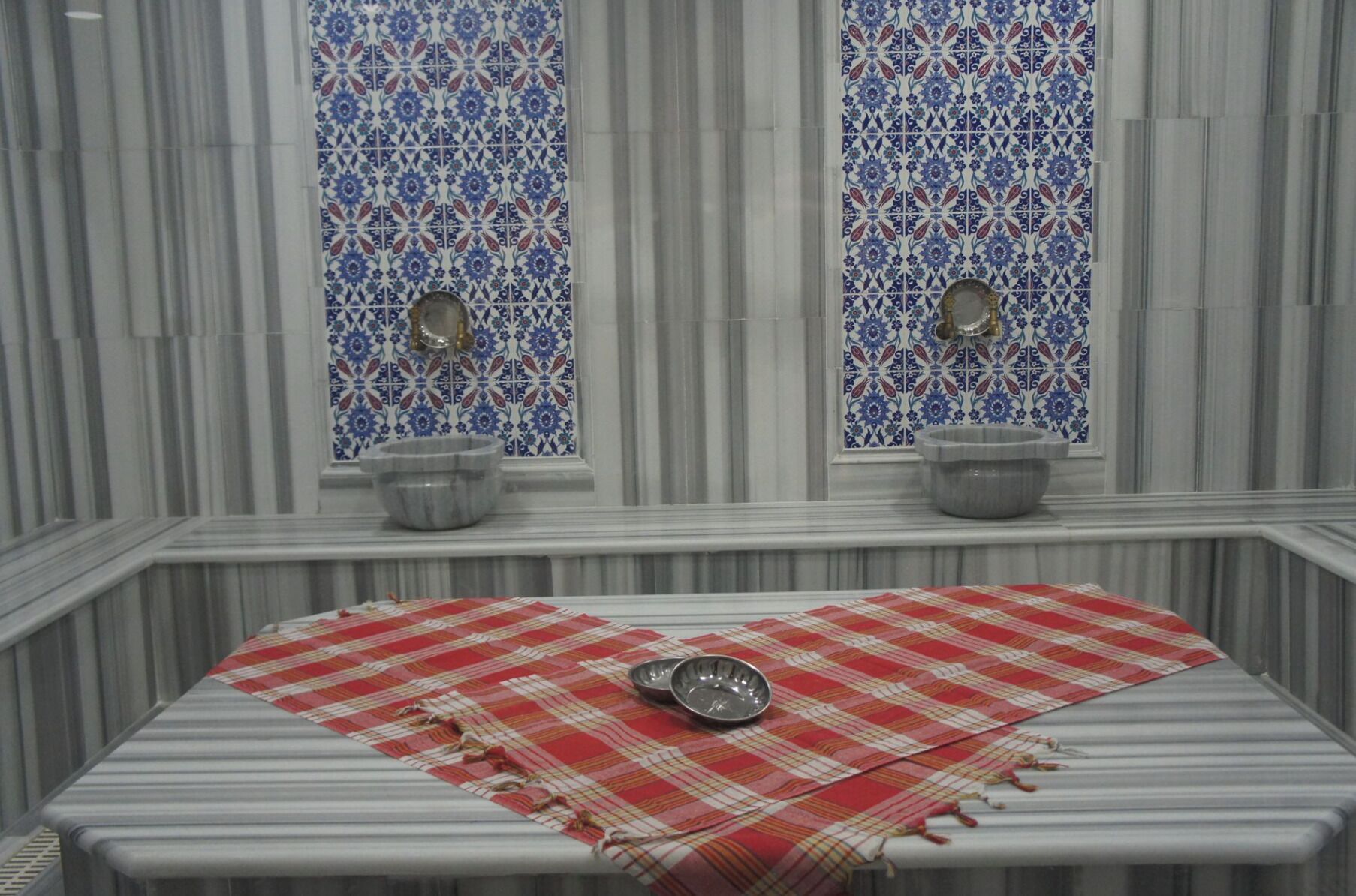 A bathroom with a striped marble wall, two windows with blue and white patterned tiles, and two sinks with mirrors.