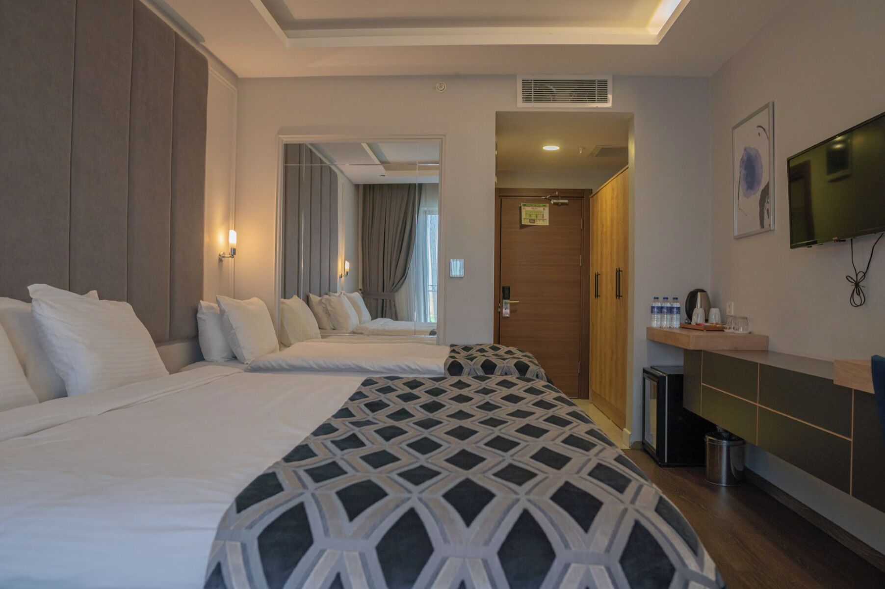 Habitación de hotel con dos camas, televisión, una kitchenette pequeña y un baño visible a través de una puerta abierta.