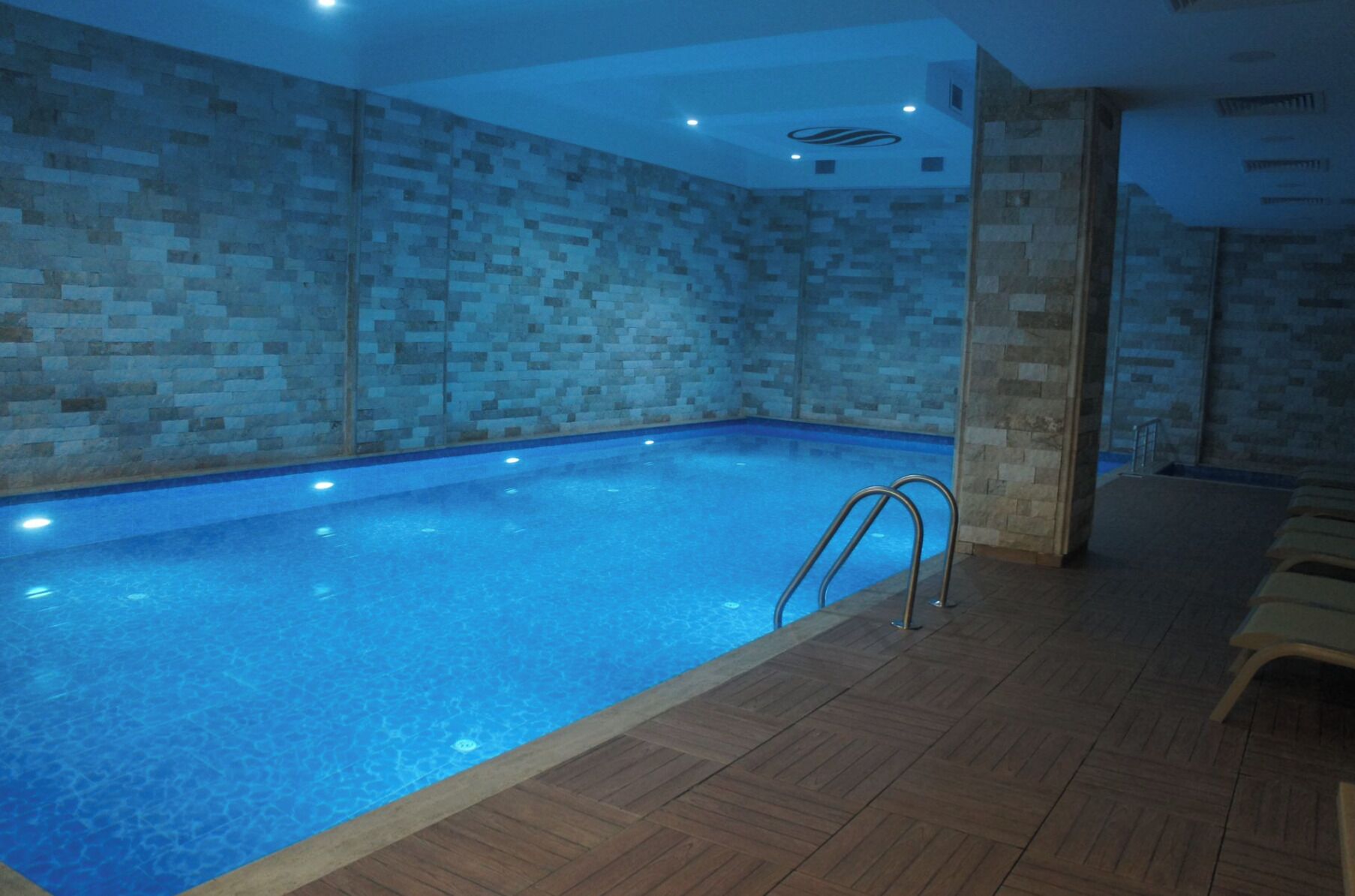 Una piscina interior con paredes de azulejos, suelo de madera y escalera de metal.