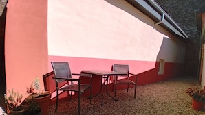 Un espace extérieur aménagé avec deux chaises et une table, entouré de plantes en pot et de gravier.